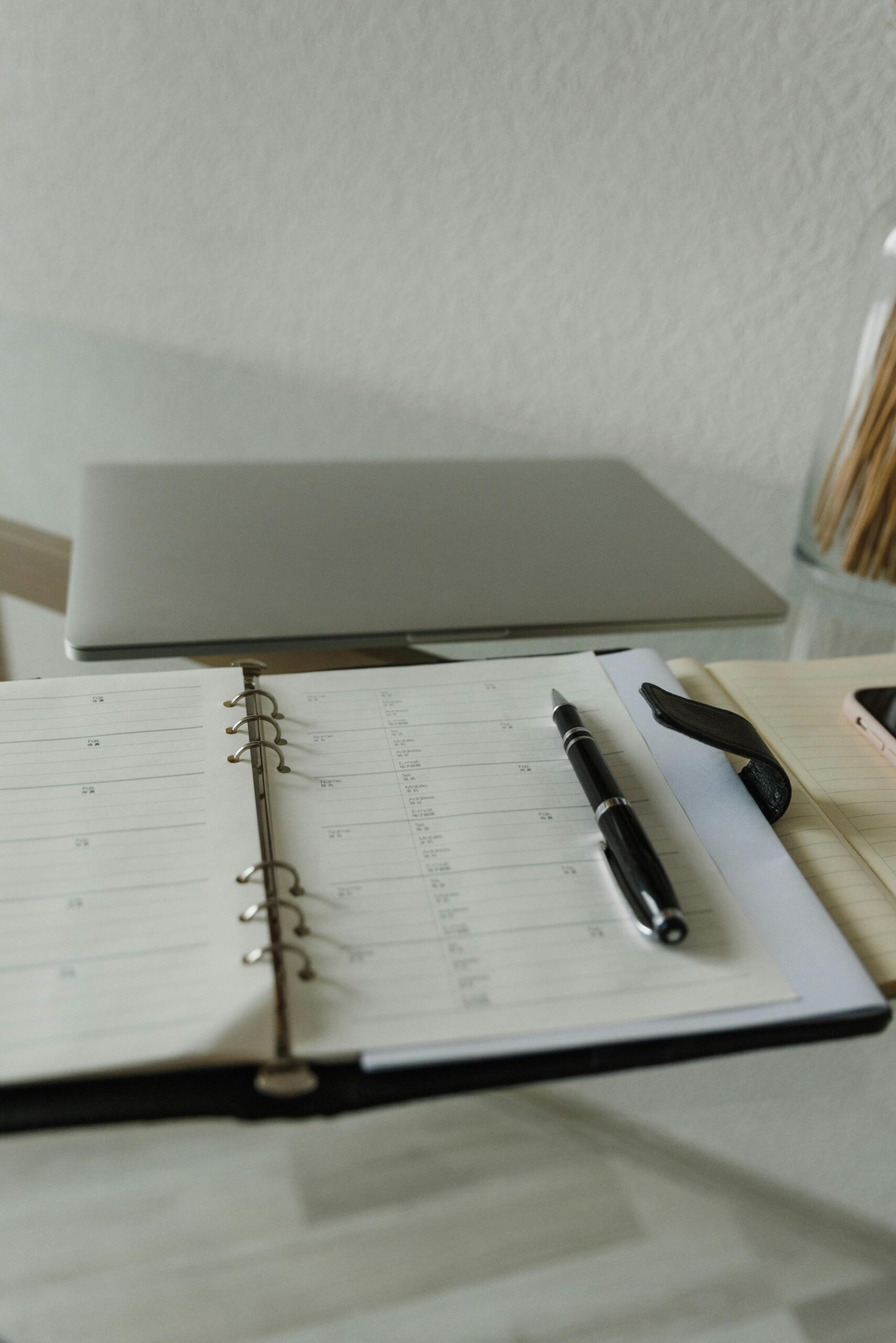 Open planner with pen on a glass desk near a closed laptop, perfect for productivity inspiration.